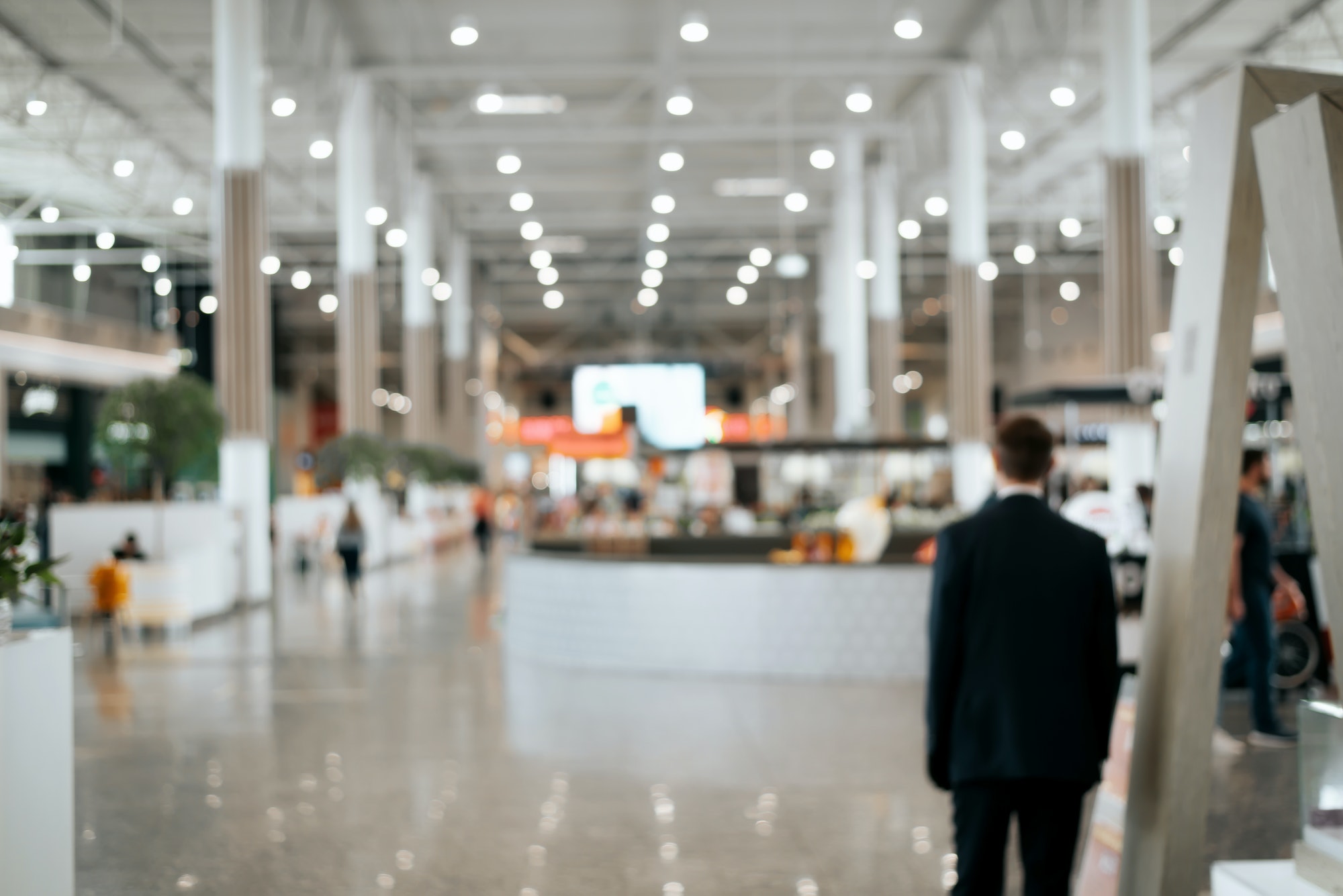 Defocused shopping mall background, large illuminated hall, security guard rear view. Blurred